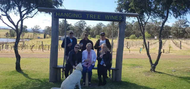 A tour group gathered under the Hanging Tree Wines archway with the vines behind
