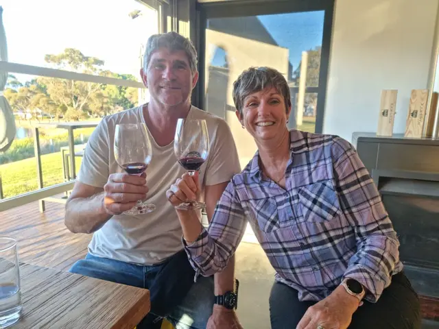 A couple raising glasses of red at a window bench looking over the vineyard