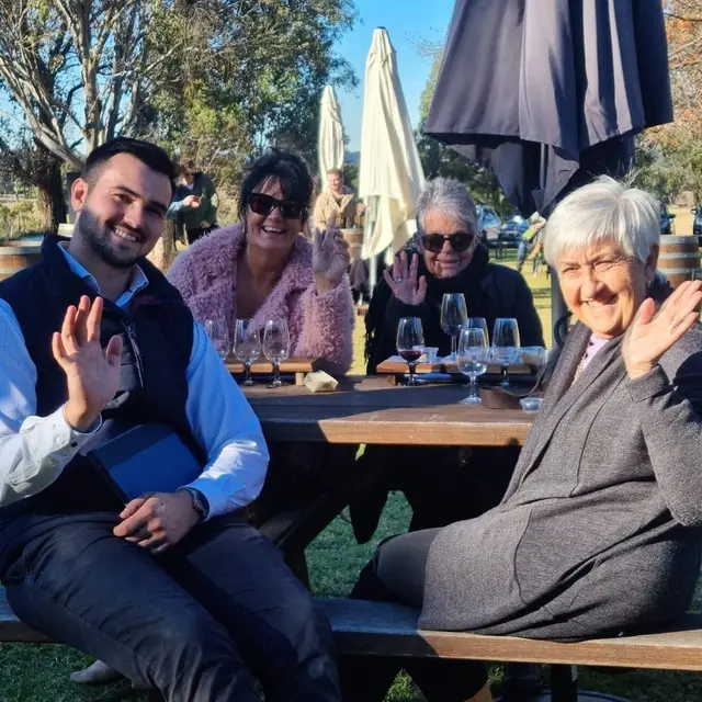 Guests waving from a shaded outdoor table during a long lunch stop