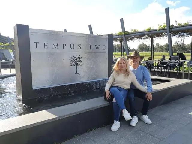 Two guests sitting on the Tempus Two entrance sign in the afternoon sun