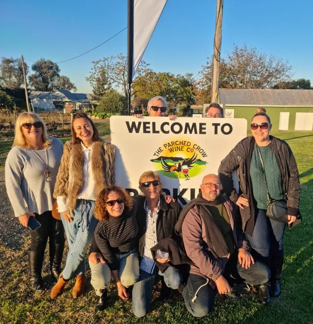 A tour group kneeling around a Pokolbin welcome sign