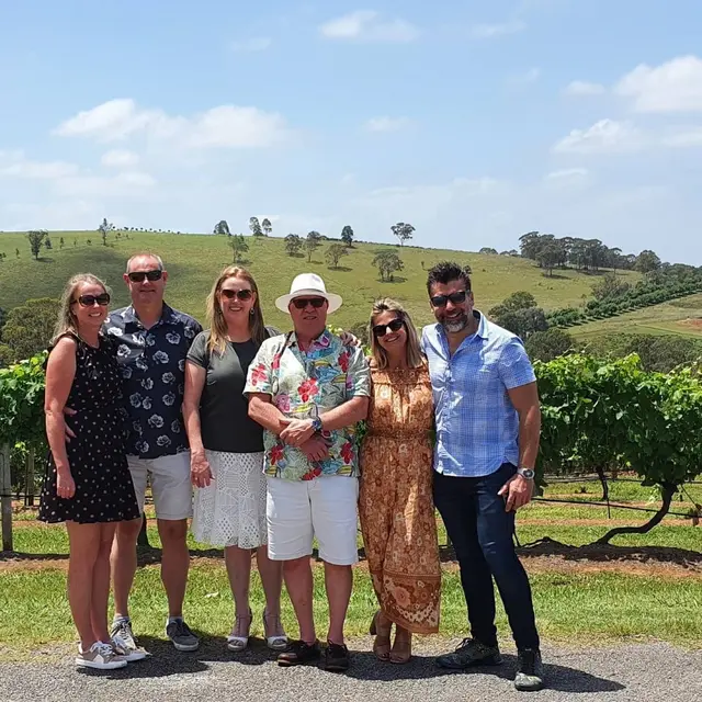 Six guests posing on a vineyard track with green hills behind