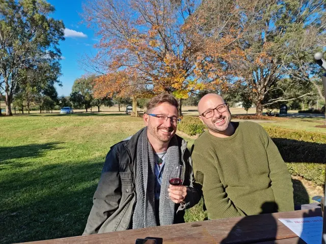 Two guests with red wine at an outdoor table under autumn trees
