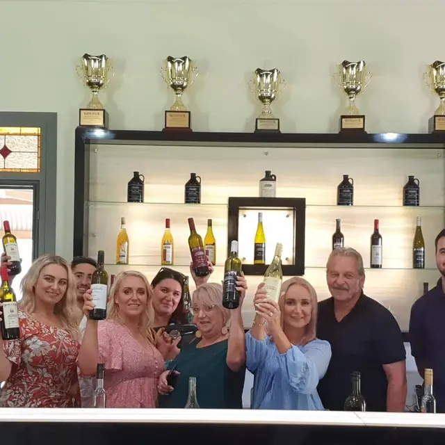 Guests raising glasses at a counter beneath a shelf of winery trophies