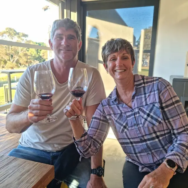 A couple raising two glasses of red at a tasting room bench