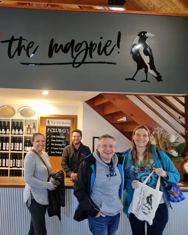 Four guests at a cellar door counter beneath a hand-painted magpie mural