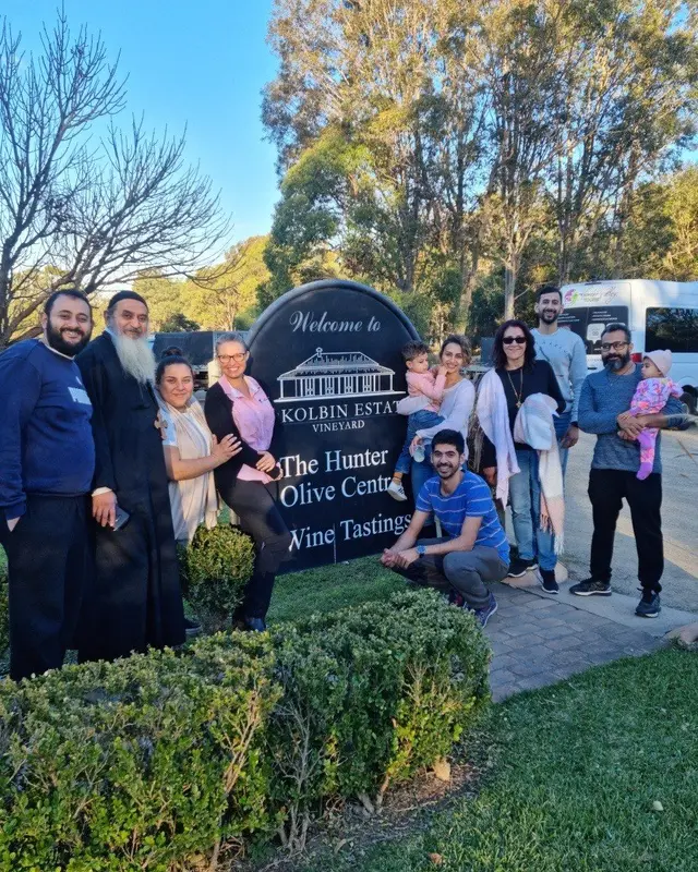 A tour group gathered around a cellar door and olive centre sign