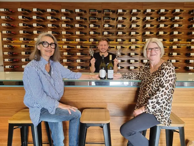Three guests at a tasting counter with a bottle wall behind them