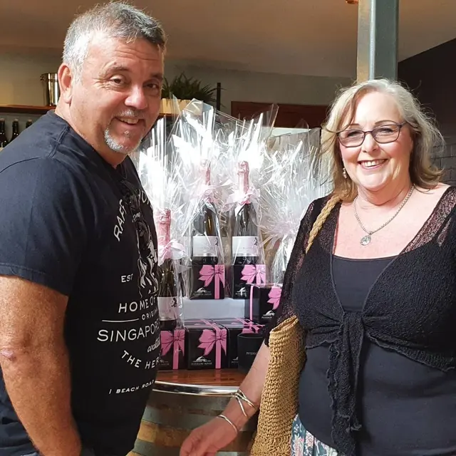 Two guests holding gift-wrapped bottles bought at a cellar door