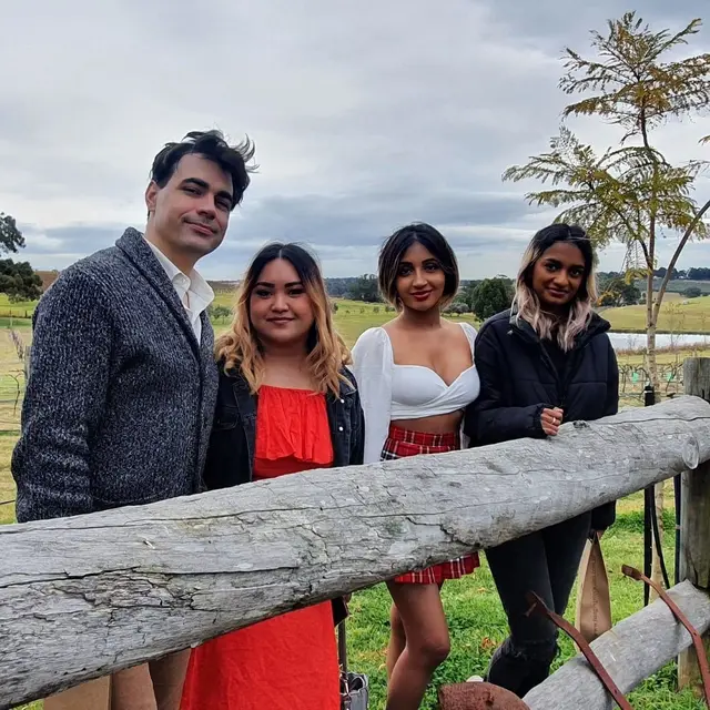 Four guests leaning on a timber fence beside the vines