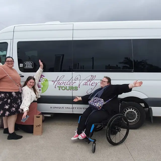 A guest in a wheelchair with arms wide beside the Hunter Valley Tours bus