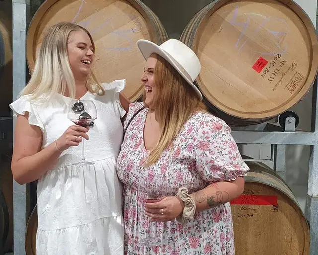 Two guests laughing together in front of stacked oak barrels