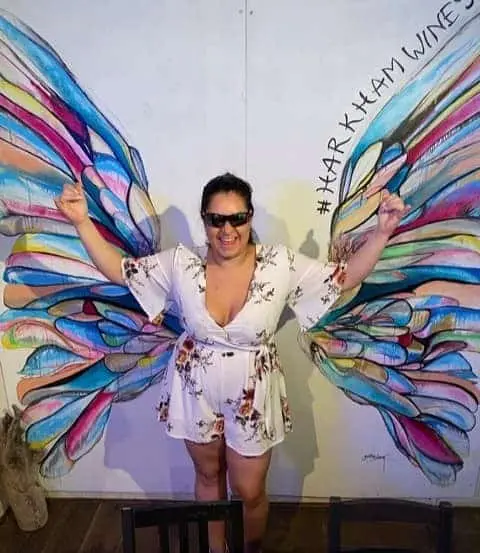 A guest posing in front of a painted butterfly-wings mural