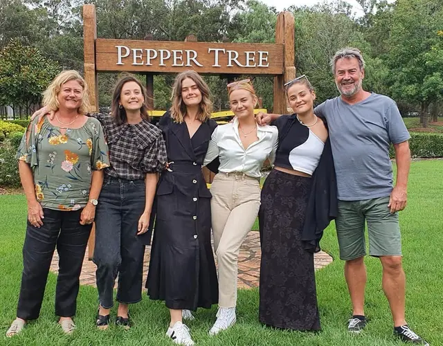 A group at the Pepper Tree sign on the lawn