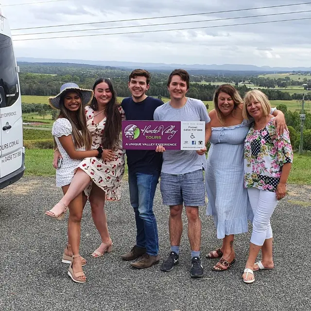 Guests holding a Hunter Valley Tours sign beside the bus