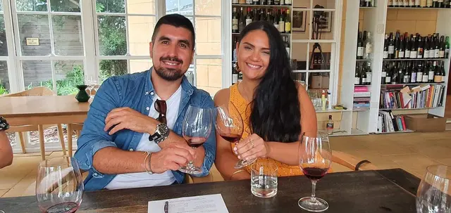 A couple at a tasting bench with the cellar door shelves behind