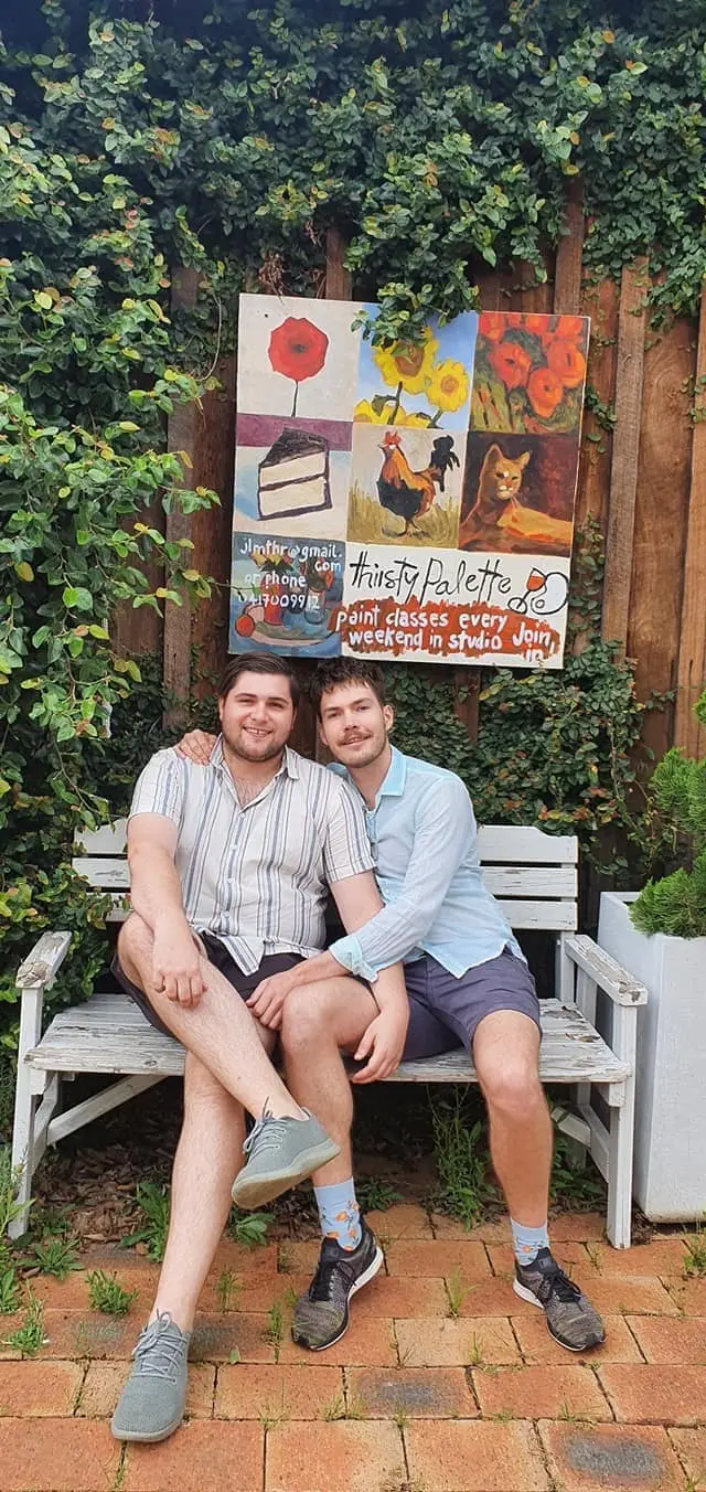 Two guests on a bench under a hand-painted menu board