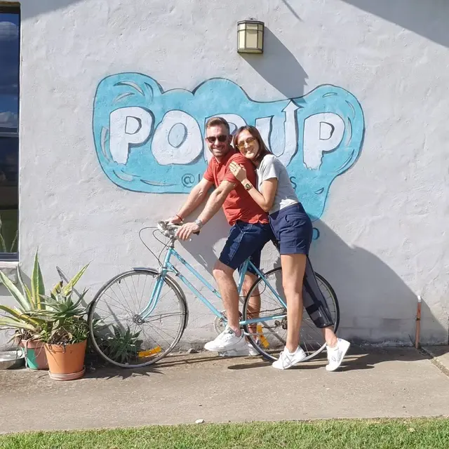 A couple posing on a bicycle in front of a painted wall mural