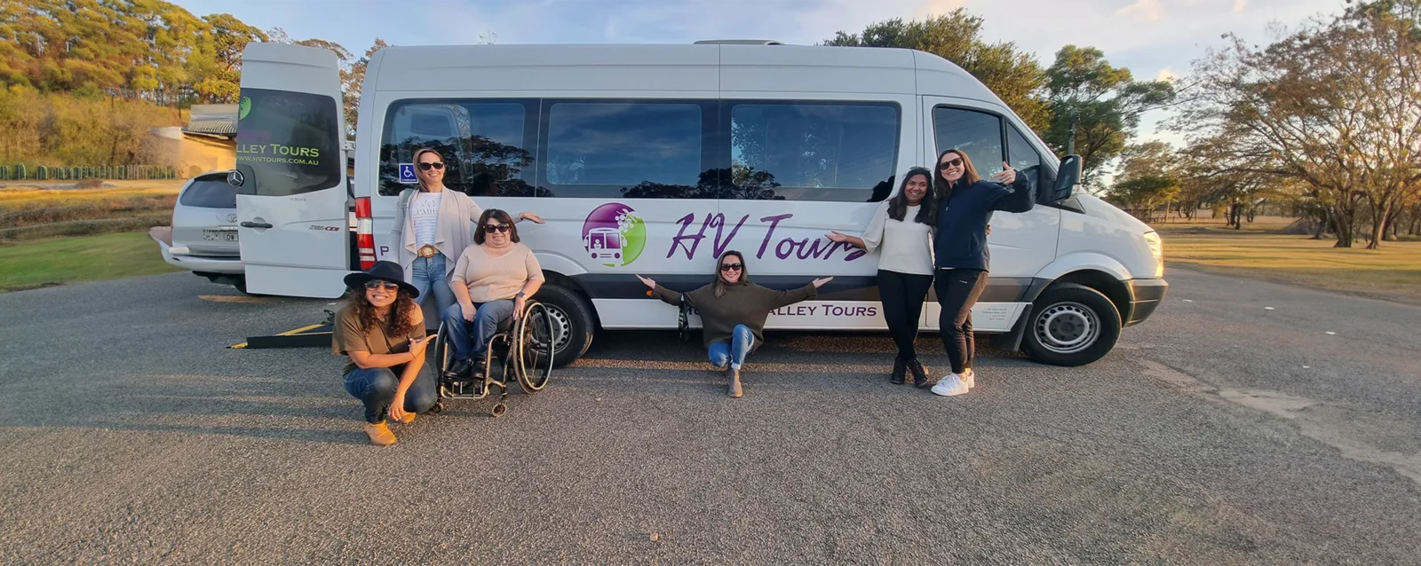 Guests, one using a wheelchair, beside the HV Tours Mercedes Sprinter with its access ramp down