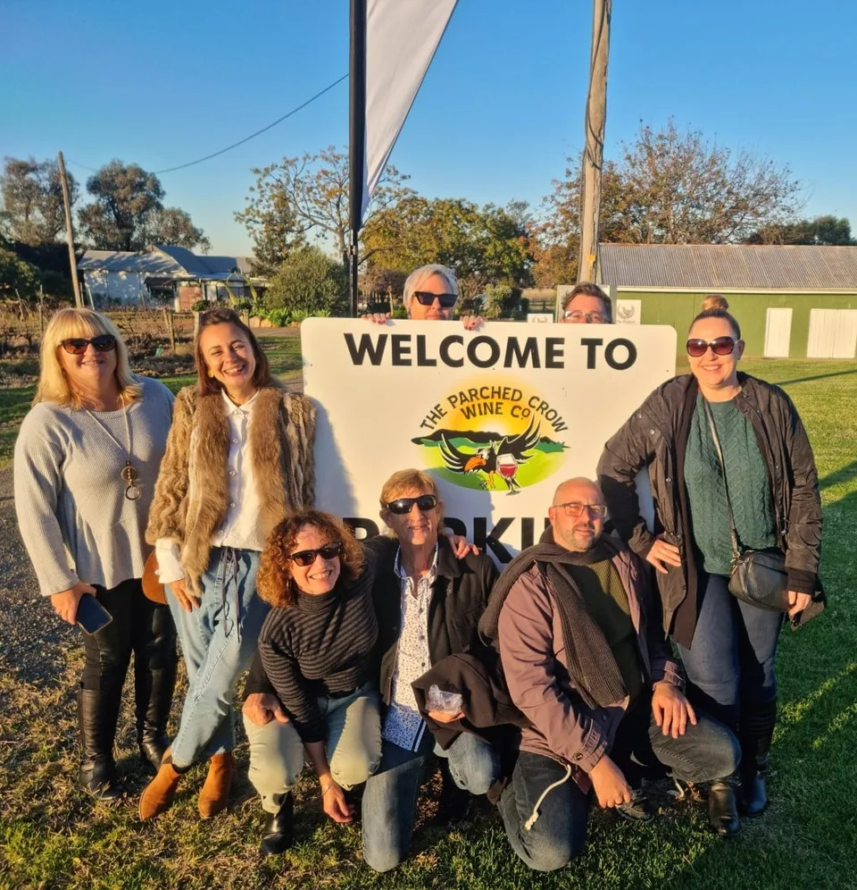 A tour group gathered at a cellar door welcome sign in Pokolbin in the late afternoon sun